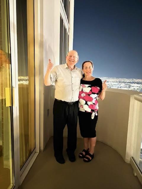 Linda and Naftali Schwartz smiling together on a city-view balcony